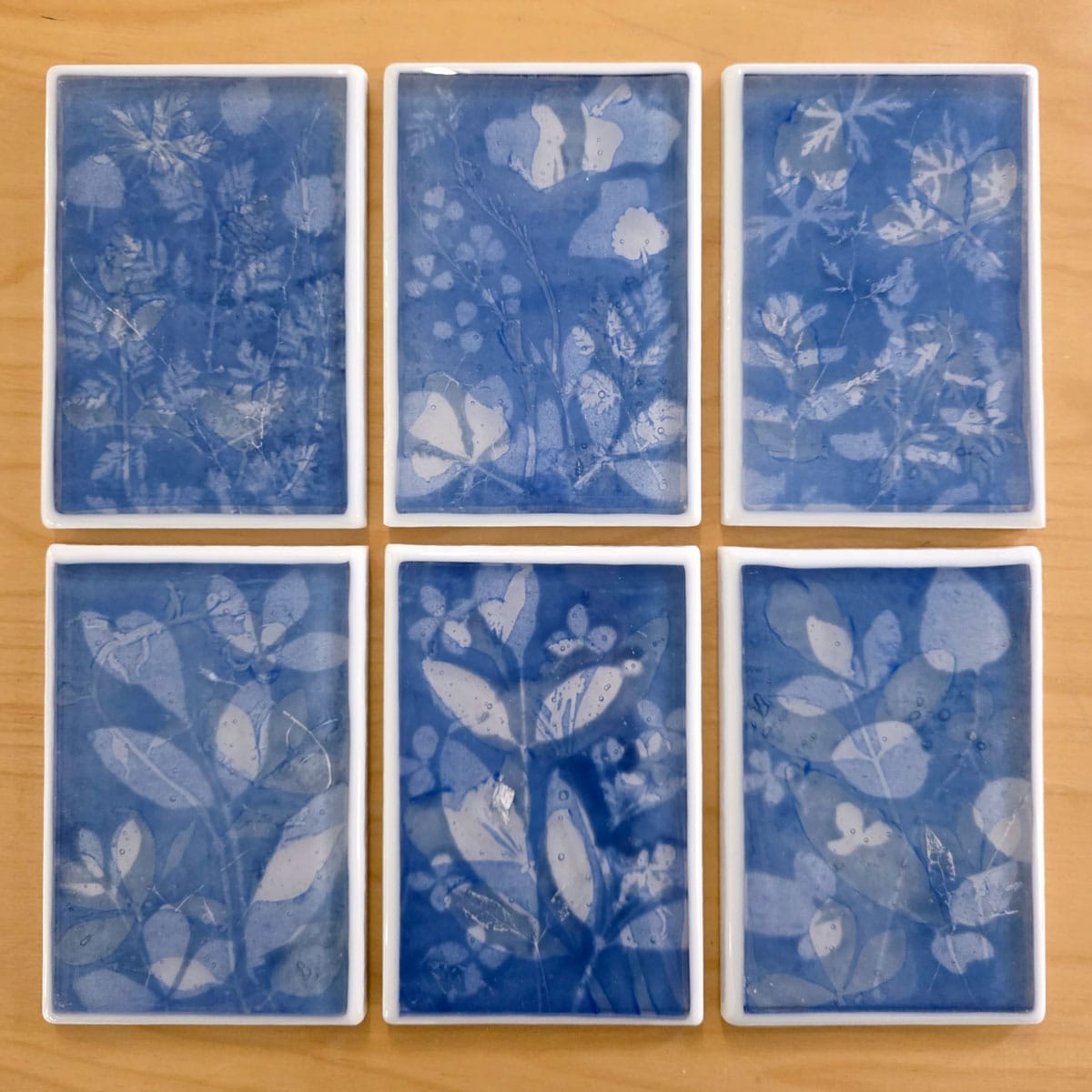 Six blue glass blocks with encased plant ash and floral patterns on a wooden surface.
